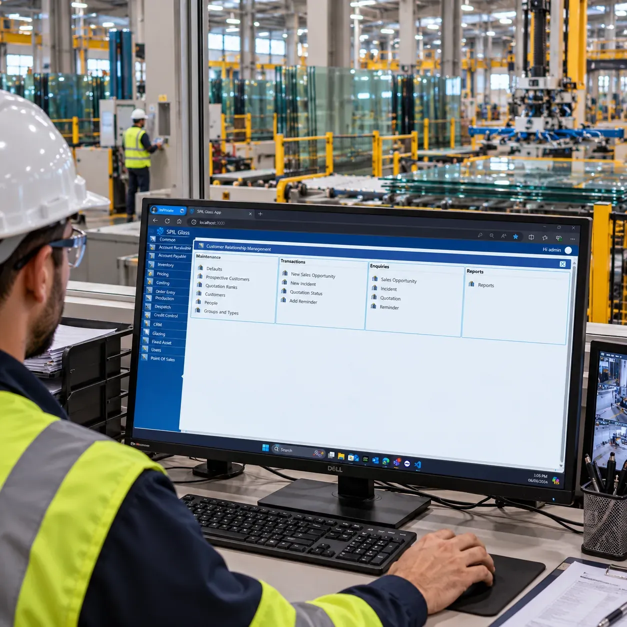 A worker in a hard hat, safety glasses and high-visibility jacket using SPIL CRM on a desktop screen on the glass factory floor